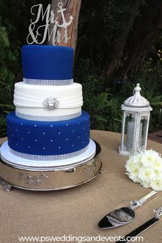 a blue and white wedding cake sitting on top of a table next to silverware