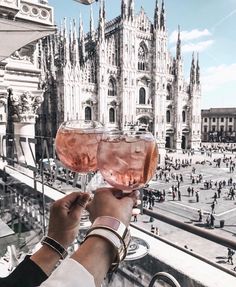 two people holding up wine glasses in front of a large building with many spires