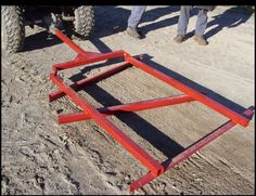 two people are standing next to a red metal frame on the ground with an atv in the background