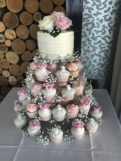 a wedding cake with cupcakes and flowers on the top is surrounded by wood slices