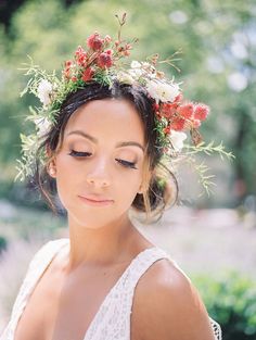 a woman with flowers in her hair wearing a white dress and holding a flower crown