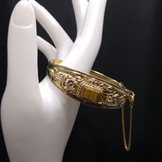 *Description: This is a beautiful gemstone hinged bracelet with safety chain from the 1940s to 1950s.  The bracelet has a layered design with filigree and then on top of this a rectangular gemstone in shades of brown.  It registers quartz on the Presidium gem tester.  The safety chain has a spring ring clasp so it may be attached or opened as designed. The bracelet clasp is a hidden box clasp and fit securely together.  This would be a great addition to your vintage jewelry collection or make a