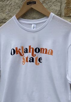 OSU Cowboys White Funky Font Long Sleeve LS Tee White School Spirit Top For Spring, White Shirt With School Spirit For Spring, White Short Sleeve Tops With Ribbed Cuffs, White Short Sleeve Top With Ribbed Cuffs, White Team Spirit T-shirt For Fall, White Stretch School Spirit Top, White T-shirt With Ribbed Cuffs For College, White Stretch Tops For School Spirit, White Stretch Tops For Game Day