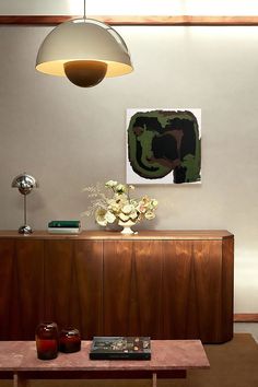 a living room with a table, lamp and pictures on the wall above it that has flowers in vases