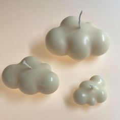 three white candles sitting next to each other on top of a table in the shape of clouds