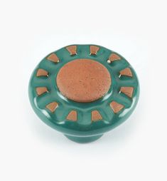 a green and brown ceramic object on a white surface with small holes in the center