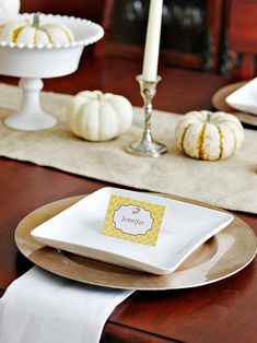 a table set for thanksgiving with white pumpkins and candlesticks in the background