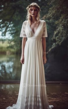 a woman wearing a white dress standing in front of a lake with trees behind her