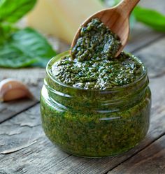 a jar filled with pesto next to garlic and basil leaves on a wooden table