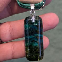 a hand holding a glass pendant with green and blue designs on it