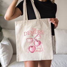 Carry the viral TikTok trend with our Very Demure Tote Bag! This cotton canvas bag features adorable coquette cherries with a pink bow paired with the "Very Demure, Very Mindful" phrase that's taken over TikTok. Perfect for coquette lovers and anyone who's all about that girly vibe, this tote is a must-have for your daily essentials. Whether you're treating yourself or gifting it to a friend, this bag is the perfect way to carry your essentials in style. Snag yours now and stay on trend! Key Fea Trendy Beige Canvas Bag For Gift, Trendy Cotton Bags For Gifts, Trendy Pink Canvas Bag As Gift, Trendy Pink Canvas Bag For Gift, Trendy Cotton Shoulder Bag Gift, Pink Girly Stuff, Coquette Bag, Viral Tiktok, Occupational Therapist