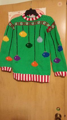 a green christmas sweater hanging on a wooden door with buttons and pins attached to it