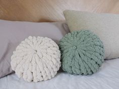 three decorative pillows on a bed with white and green colors, one is made out of yarn