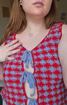 a woman wearing a red and blue crochet top holding her hands on her chest