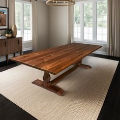 a large wooden table sitting on top of a rug in a living room next to two windows