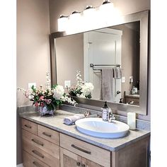 a bathroom sink sitting under a large mirror next to a counter top with flowers on it