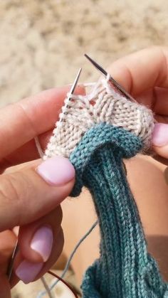 someone is knitting something with yarn on the beach in front of their feet and hands