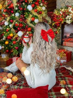 a woman sitting in front of a christmas tree holding a coffee mug with a red bow on her head