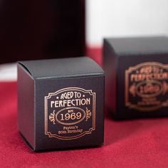 two black boxes with gold lettering on them sitting on a red cloth covered tablecloth