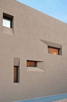 two windows on the side of a building with concrete walls and blue sky in the background