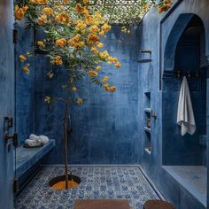 a blue bathroom with yellow flowers hanging from the ceiling and a tree in the corner