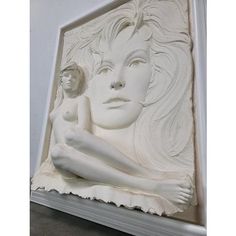 a white sculpture sitting on top of a table next to a wall mounted plaque with a woman's face