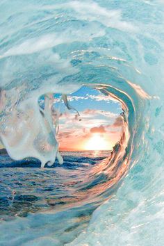 an ocean wave with the sun setting in the background