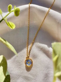 "This dainty, gold, Forget Me Not necklace is the perfect accessory to bring a touch of charm to your outfit. It's also a perfect gift for the flower lovers in your life! Real, pressed, Forget Me Nots are gently arranged inside the gold, circle bezel. They are then preserved in resin to create this timeless and delicate statement. This minimalist pendant is lightweight, and can be worn all day without discomfort! They are made with hypoallergenic gold plated 18\" chain and crystal clear resin, a Blue Flower Charm Jewelry As Gift For Her, Blue Gold-plated Charm Necklace With Adjustable Chain, Blue Adjustable Flower Necklace For Gift, Adjustable Blue Flower Necklace For A Gift, Delicate Blue Necklace With Adjustable Chain, Dainty Blue Necklace For Her, Blue Flower-shaped Jewelry For Her, Gold Flower Pendant Necklace With Adjustable Chain, Adjustable Gold Necklace With Birth Flower