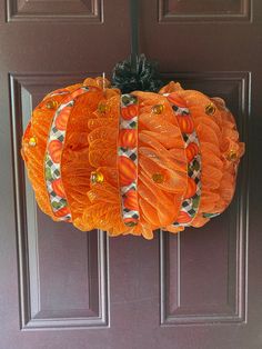 an orange pumpkin hanging on the front door with decorative ribbon around it's sides