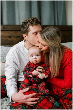 a man and woman kissing their baby on the cheek while sitting in bed with plaid sheets