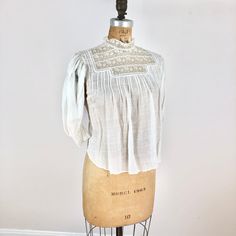 "Antique Edwardian white check cotton blouse has a lace yoke, pin tucks at the bust, and lace trimmed sleeves. The blouse has pin tuck down the length of the back, buttons for closure and a tie at the waist. Condition Overall good condition, has a stain at the back right shoulder area, tiny-small holes around the right sleeve shoulder area, a small hole near the back right pit seam, and a pink-ish stain near the shoulder. There's also a tiny hole near the back left shoulder. There's also a pink Lace Insert Blouse, Cotton Tops With Pintucks For Daywear, Vintage White Tops With Lace Trim For Daywear, Cotton Peasant Top With Lace Trim For Daywear, Lace Collar Top For Daywear In Fall, Fall Lace Top With Lace Collar For Daywear, Fitted Cotton Peasant Top With Lace Trim, Fitted Cotton Peasant Top, White Lace Collar Top For Daywear