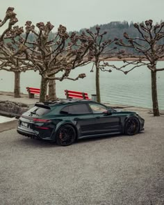 a black sports car parked in front of some trees near the water with red benches