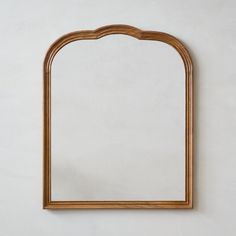 a wooden mirror hanging on the wall next to a white wall with a plant in it