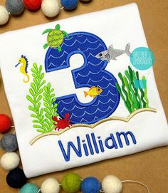 a birthday shirt with an ocean theme and the number three on it, surrounded by pom - poms