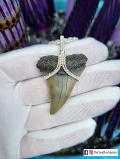 a person holding a piece of jewelry in their hand with purple feathers behind it and an arrow shaped pendant hanging from the middle