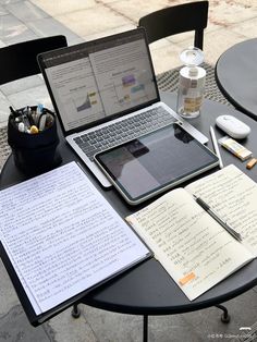 an open laptop computer sitting on top of a table next to notebooks and pens