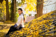 a woman sitting on top of a bench covered in yellow leaves and looking at the camera