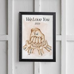 a framed poster with the words we love you and two hands holding each other in front of a white door