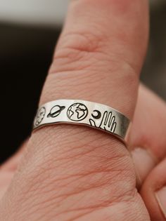 a person's hand with a silver ring that has the words and symbols on it