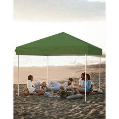 a group of people sitting under a green tent on the beach