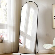 a large mirror sitting on top of a wooden floor next to a white chair in front of a window