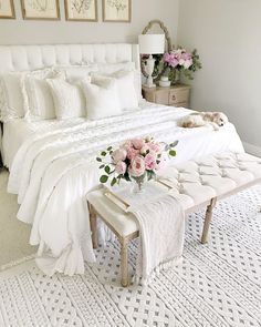 a bedroom with white bedding and pink flowers on the foot stools in front of the bed