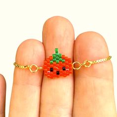 a hand holding a small orange beaded bracelet on it's fingers and wearing a gold chain