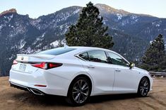 a white car parked on top of a dirt road in front of some trees and mountains