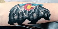 a bear tattoo on the arm with mountains and sun in the sky behind it's head