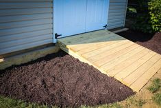 a wooden walkway leading to a blue door in the back yard with mulch on the ground