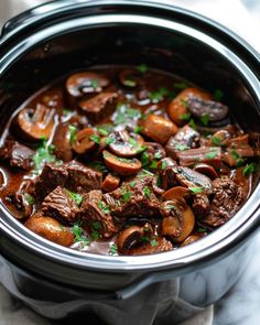 a crock pot filled with beef and mushrooms, garnished with parsley