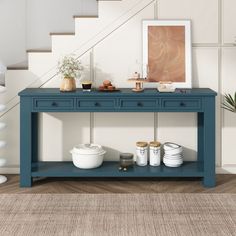 a blue console table with two drawers under the stairs and some white vases on top