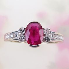 A vibrant natural ruby is centered on this attractive 14k white gold diamond ring. The .65 carat ruby is of deep raspberry pinkish-red color. It measures 6.5mm x 5mm x 2.5mm and is tightly held by two half-bezels.  Four bright and sparkly 2mm .03 carat diamonds flank the red gem. The shoulders are channel set with four 1.5mm diamonds (eight qty. with .12 carat total weight). Collectively, the ring has an estimated total weight of .25 carat or 1/4 carat. The inside is signed, "STS" (STS Jewelry Co., based in Austin, TX) and hallmarked "14k" (white gold). Please see detailed measurements below. The ring is in beautiful condition and would be lovely as an engagement ring or everyday statement ring. Wt: 2.5 grams US Ring size : 6.75 Length: 7.5mm or just over 1/4 Inch Width: 20mm or 13/16 Inch 14k White Gold Diamond Ring, Half Bezel, Pinkish Red, 14k White Gold Ring, Channel Set, White Gold Ring, Natural Ruby, Deep Red, White Gold Diamonds