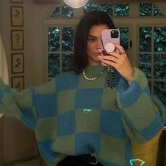 a woman taking a selfie in front of a mirror wearing a green and blue checkered sweater